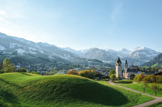 Kitzbühel church above green meadows with mountains behind