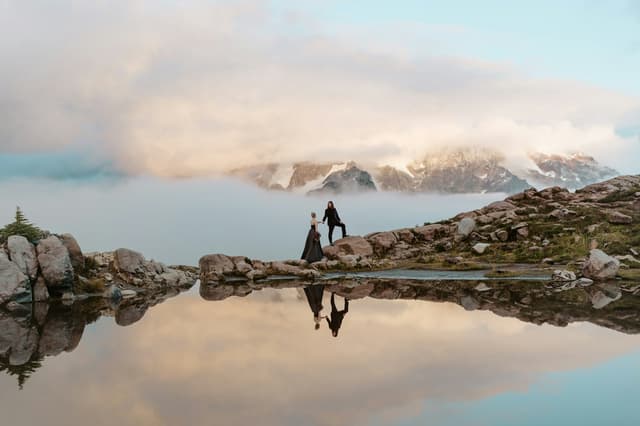 Couple in wedding clothes on rocks above a mountain lake