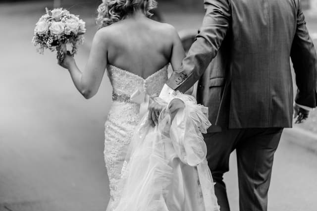 Black-and-white photo of a bride and groom walking away arm in arm